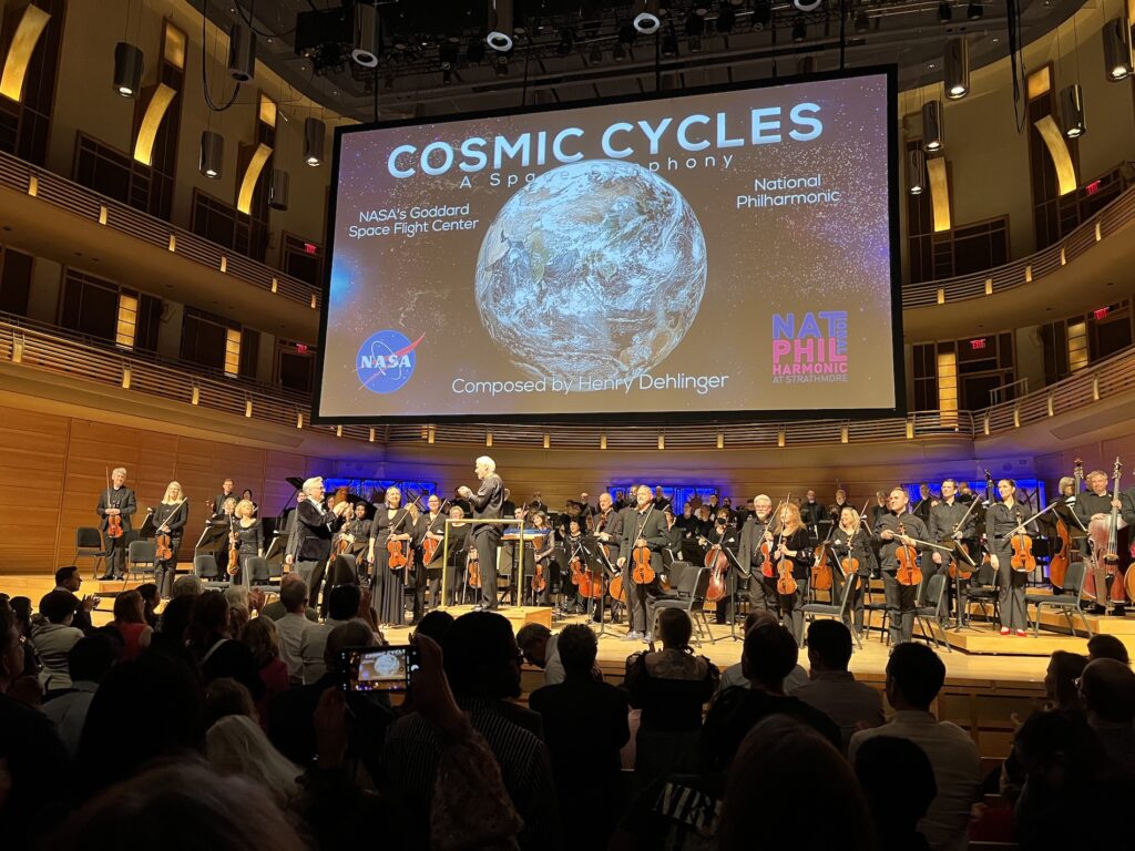 Large screen at the Strathmore, a photo of earth from space. Text: Cosmic Cycles a space symphony