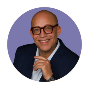 Profile Photo of Todd Tolson, a fair skin black male with a shaved head, wearing red framed glasses, bright blue eyes and a gleaming smile.