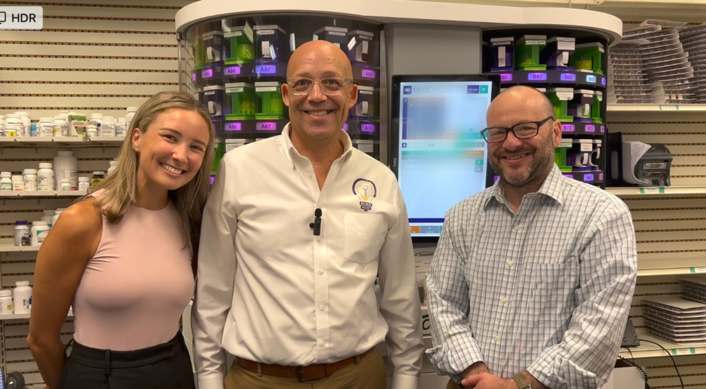 Todd with the senior staff of Accessible pharmacy services pose for a photo in front of a very large pill organizer machine