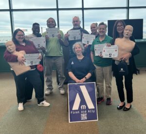 Christine the instructor sits as her students stand behind her holding their completion certificates for Red Cross CPR, AED and First Aid Training and Certification