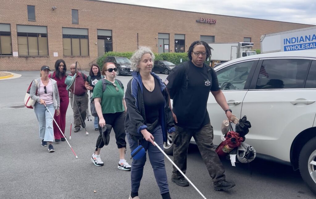Trouble Defense LLC instructors walk with a group of blind and low vision students to the gun range. Some students are using white cane.