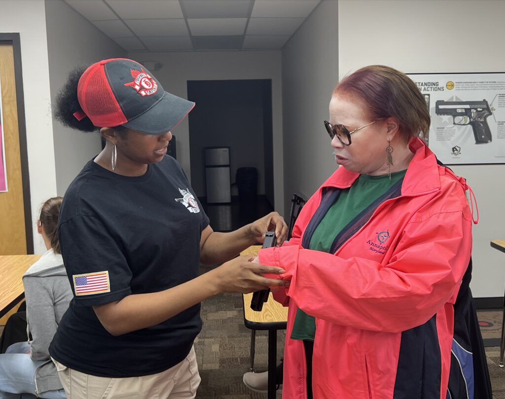 A firearms instructor works with a low vision student as she touches a firearm.