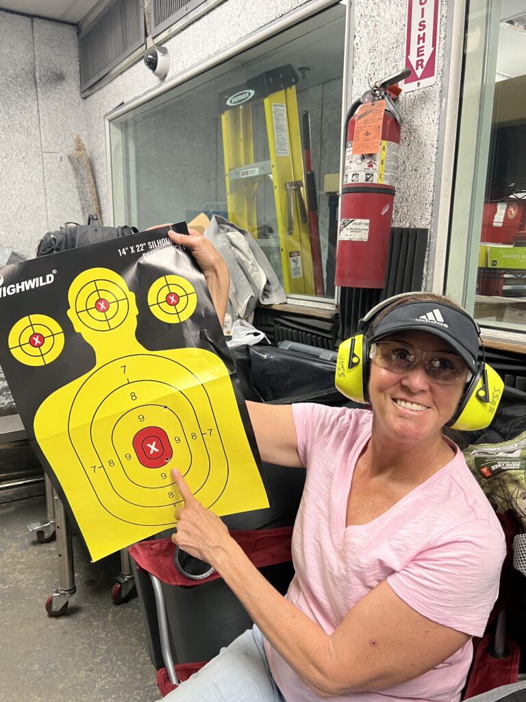 A blind woman holds up her target, pointing to the bullseye she hit.